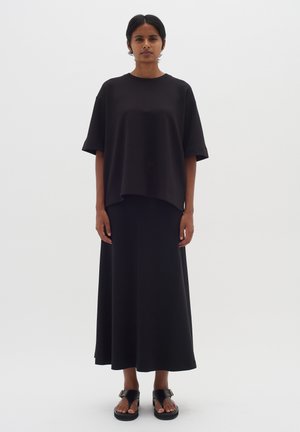 Black oversized short-sleeve top paired with a long black skirt. Simple design, smooth texture, complemented by flat black sandals.