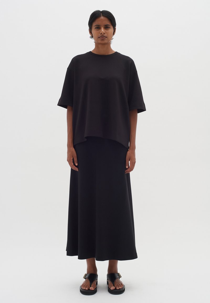 Čierny oversized top s krátkym rukávom v kombinácii s dlhou čiernou sukňou. Jednoduchý dizajn, hladká textura, doplnené o ploché čierne sandále.