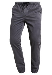 Pantalon de jogging gris léger avec une taille élastique et un cordon de serrage, doté de poches latérales et de chevilles resserrées. Texture lisse.