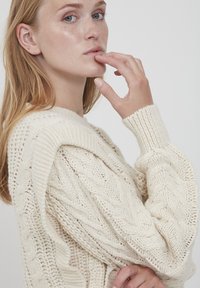 Maglione lavorato a maglia a treccia color crema con scollo rotondo, motivo testurizzato, polsini a coste e vestibilità rilassata, realizzato in spessa e voluminoso filato.