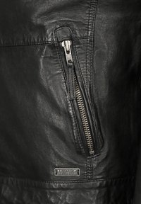Schwarze Lederjacke mit einer diagonalen Reißverschlusstasche, strukturiertem Finish und einem silbernen Hardware-Akzent mit einem "MUSTANG"-Logo.