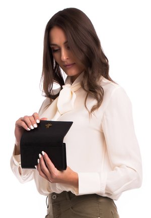 Portafoglio nero in pelle con una texture liscia, che presenta un emblema dorato a forma di ape, tenuto da una persona con una camicetta crema.