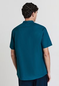 Kurzarmhemd aus dunkelblauem Stoff mit glatter Textur und einem Knopfkragen. Verfügt über ein sauberes, gerade geschnittenes Rückendesign.