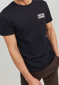 Musta puuvillainen t-paita, jossa vasemmassa rinnassa valkoinen "JACK & JONES" -logo, pyöreä pääntie ja lyhyet hihat. Sileä pinta.