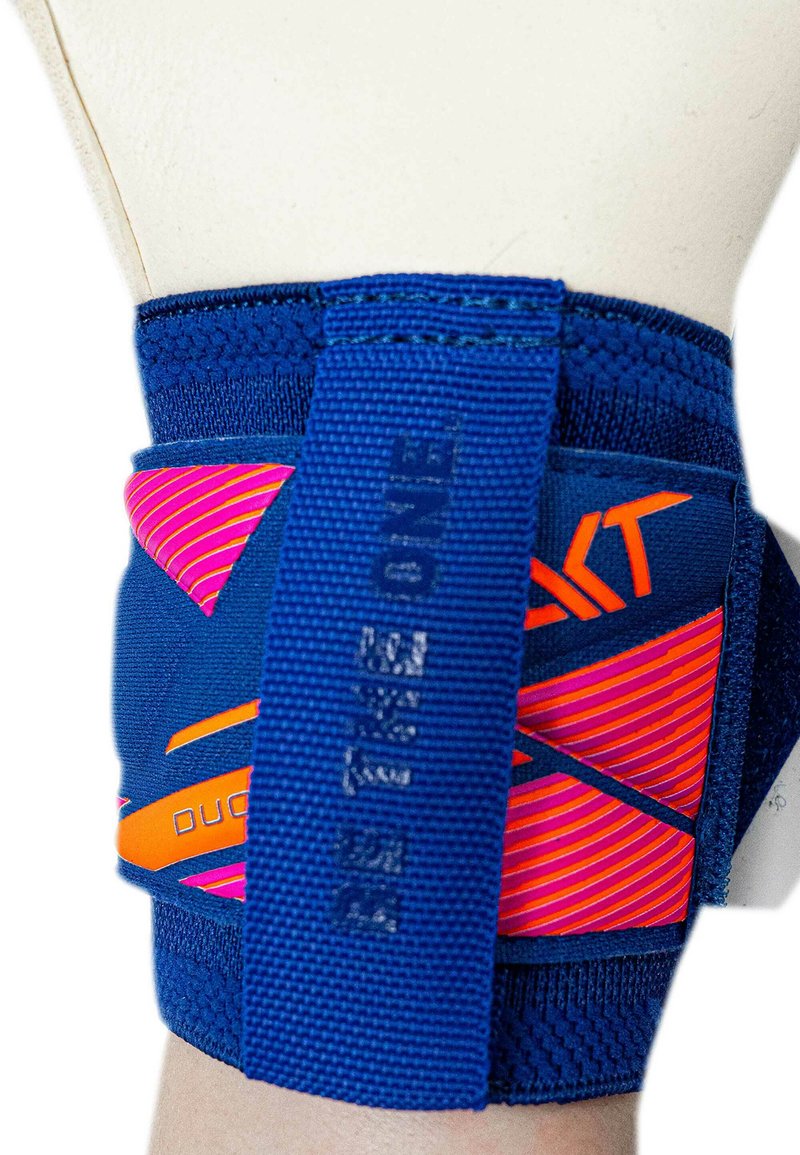 Blue and orange wrist support brace with adjustable straps and pink diagonal stripes, worn on a beige mannequin arm.