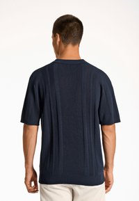 Tummansininen lyhythihainen neulepusero, jossa on ribbikuvio ja pystysuora raidoitus. Varustettu klassisella kauluksella ja sivuviillolla helman kohdalla.