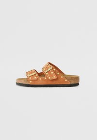 Sandales en daim tan avec deux sangles ajustables, clous dorés et semelle en liège. Semelle en caoutchouc noire. Design minimaliste.