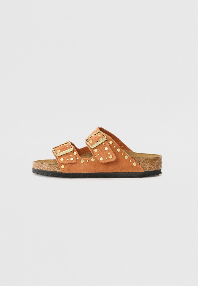Sandales en daim tan avec deux sangles ajustables, clous dorés et semelle en liège. Semelle en caoutchouc noire. Design minimaliste.