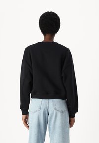 Melna sporta krekls ar brīvu piegriezumu, ribota piedurknes un apakšmala, savienots ar gaiši ziliem augsto jostasvietu džinsiem ar klasisku piecu kabatu dizainu.