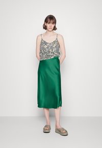 Camisola de alças finas com estampado floral, combinada com uma saia de cetim verde sólida. A saia tem uma textura suave e cai até à metade da panturrilha.