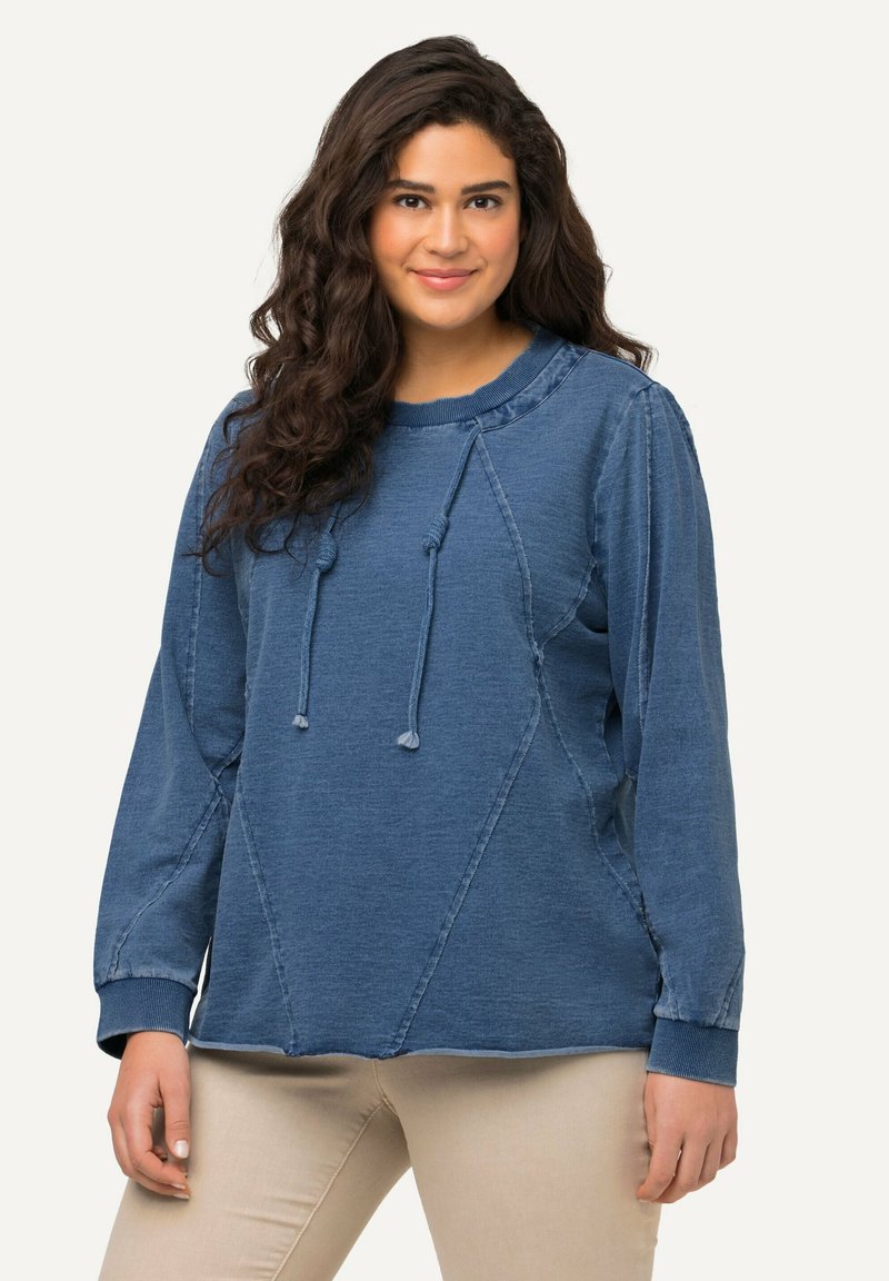 Modrá mikina s kapucí, stahovací šňůrkou, dlouhými rukávy a švy. Vyrobena z měkké látky, s volným střihem a žebrovanými manžetami.