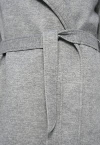 Γκρι παλτό τύπου wrap με απαλή υφή, που διαθέτει ζώνη στη μέση, γωνιακό γιακά και διακριτικό ανάγλυφο μοτίβο.