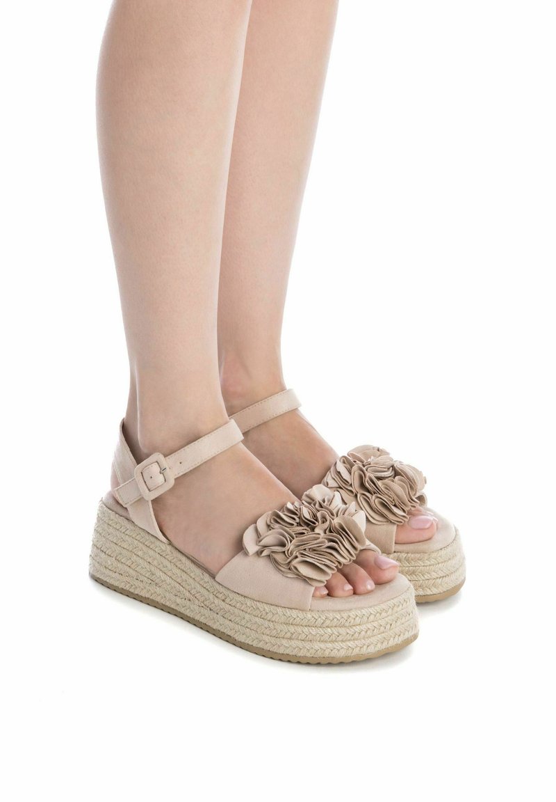 Sandalias de plataforma de esparto en tejido beige con detalle de volante floral, correa ajustable en el tobillo y suela con textura de paja.