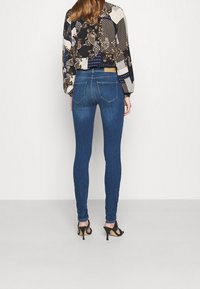 Vaqueros ajustados de color azul con una cintura de altura media, que cuentan con bolsillos traseros tradicionales y se combinan con una blusa corta con estampado y tacones altos negros.