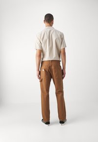 Camicia beige a maniche corte e pantaloni cargo marroni con tasche. Tessuto testurizzato e taglio dritto. Scarpe con motivo bianco e nero completano il look.