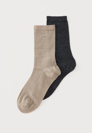 En beige og en mørkegrå ribbet crew sok, parret og placeret side om side på en ensfarvet baggrund.