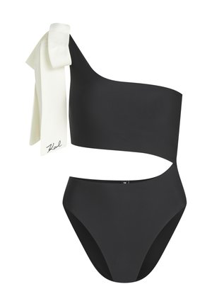 Maillot de bain noir asymétrique avec une découpe à la taille et un nœud blanc noué sur l'épaule, arborant une petite signature.