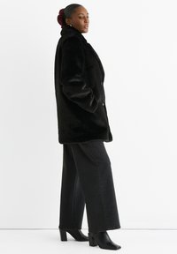 Black faux fur coat with a high collar and front buttons, paired with black wide-leg jeans and black heeled ankle boots.