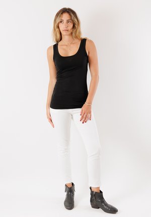 Top senza maniche nero con scollatura a barco, abbinato a pantaloni bianchi aderenti e stivali alla caviglia. Tessuto liscio, senza fantasie, design minimalista.
