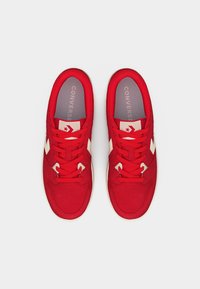 Paire de baskets Converse rouges avec logos étoile-chevron blancs et lacets rouges, vues de dessus sur un fond uni.