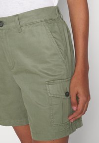 Pantaloni cargo verdi in cotone misto, caratterizzati da tasche laterali, chiusura con bottone e una vestibilità rilassata con dettagli cuciti e tessuto testurizzato.