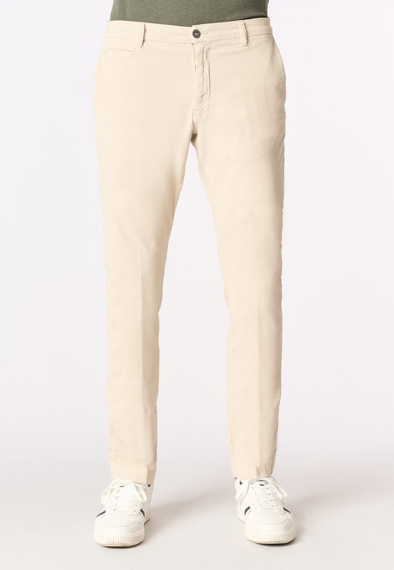 Chinos beige chiaro in cotone, con una vestibilità slim, tasche frontali e chiusura con zip e bottone. Abbinati a sneaker bianche.