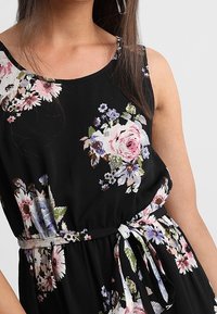 Černé květinové šaty s květinovým vzorem v růžové, bílé a fialové barvě. Mají kulatý výstřih a pásek v pase, který podtrhuje siluetu.