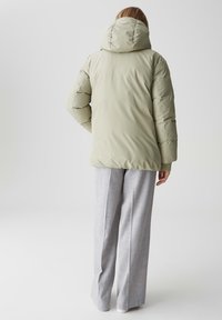 Giacca puffer di color verde salvia chiaro, con cappuccio, design trapuntato e dettagli a coste sui polsini, abbinata a pantaloni grigi a gamba larga.