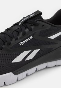 Čierna športová obuv s prednou časťou z textilu, s logom Reebok a bielymi akcentmi. Obsahuje hrubú podrážku s textúrovaným, segmentovaným dizajnom pre lepšiu priľnavosť.