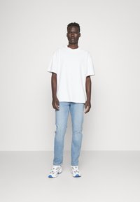 White oversized t-shirt, light blue jeans, and multicolored sneakers. The fabric is smooth; t-shirt features a round neckline, casual fit.
