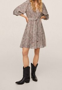 Kukallinen mekko vaaleissa sävyissä, jossa on kolme neljännesosa hihoja ja vyötäröä korostava leikkaus, yhdistettynä mustiin nahkaisiin cowboy-korkokenkiin.