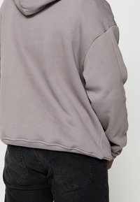 Šedá mikina s kapucí, v uvolněném střihu a s žebrovanými manžetami. Vyrobena z měkké tkaniny, bezšvový design na ramenou a zádech.