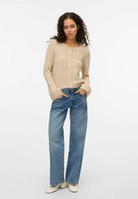 Cardigan beige en tricot avec un col rond et une fermeture par boutons, associé à un pantalon en jean large bleu clair et des bottines crème.