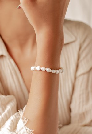 Pearl bracelet on a wrist; features round white pearls with a smooth texture, evenly spaced, against a subtle background.