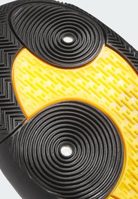 Zwarte en gele rubberen schoenzool met een gestructureerd grippatroon, gekenmerkt door ronde indrukken en een glad centraal gedeelte.