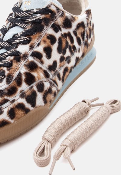 Αθλητικό παπούτσι με ανώτατο μέρος σε σχέδιο λεοπάρδαλη και μαύρα κορδόνια, συνοδευόμενο από ένα επιπλέον ζευγάρι μπεζ κορδόνια πάνω σε λευκό φόντο.