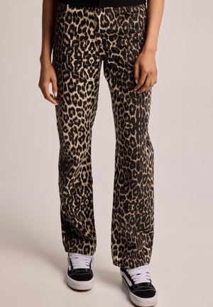 Leoprint-Hose mit geradem Bein, getragen mit schwarz-weißen Sneakers und weißen Socken vor neutralem Hintergrund.