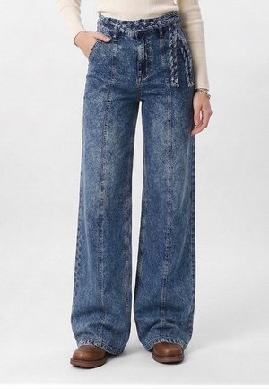 Vide bena jeans i falmet blå med høyt liv, flettet belte, frontlommer, brukt med brune sko og en kremfarget langermet topp.