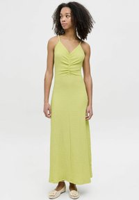 Robe maxi vert citron avec un tissu texturé, dotée de fines bretelles spaghetti et d'un décolleté froncé ; associée à des chaussures plates de couleur claire.