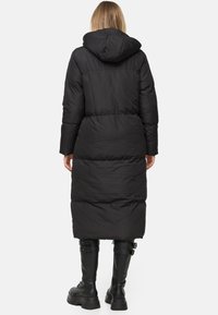 Zwarte pufferjas met een capuchon, lange lengte, gezepte textuur en een cinched taille; gecombineerd met kniehoge zwarte laarzen met gespen.