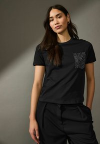 T-shirt nera in cotone con maniche corte e scollatura rotonda, caratterizzata da un design della tasca testurizzato con motivi astratti.