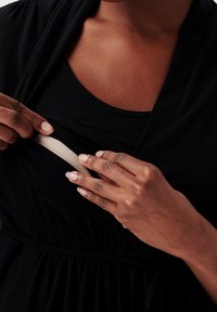 Czarna odzież o kroju z drapowaniem i elastycznym paskiem, odsłaniająca jasną wewnętrzną warstwę, która jest odciągana na bok, podkreślając jej warstwową konstrukcję.