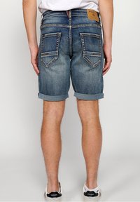Denim shorts in a light blue wash, featuring rolled cuffs, two back pockets with pointed flaps, and a tan label at the waist.