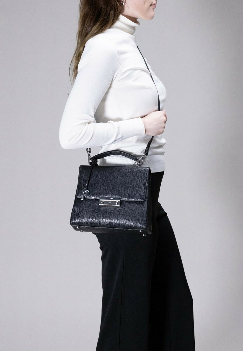 Schwarze Lederhandtasche mit strukturierter Form, strukturiertem Finish, silbernen Beschlägen und abnehmbarem Tragegurt. Auffälliges Schließdetail an der Vorderseite.