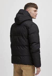 Svart dunjakke med hette, med quiltede seksjoner og en glattere, jevn tekstur. Designet er minimalistisk og moderne.