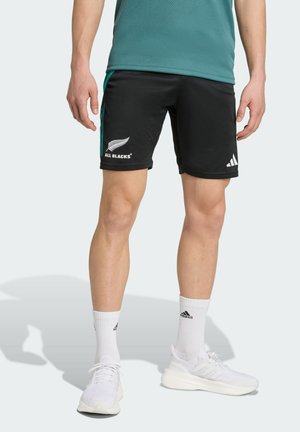 Sorte træningsshorts med teal detaljer, udstyret med "ALL BLACKS" logoet og et Adidas logo. Bæres med hvide sokker og hvide sneakers.