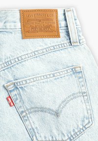 Jeans de denim azul claro con un parche de cuero etiquetado "Levi Strauss & Co." y una etiqueta roja en el bolsillo trasero, con un diseño de costura clásico.