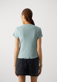 Haut bleu clair à manches courtes avec une texture côtelée et un ourlet légèrement en dentelle, associé à une mini jupe en denim noire avec des bords effilochés.