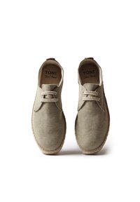 Scarpe in tela beige con finitura strutturata, punte arrotondate e suola in juta intrecciata. Presentano un design con lacci e un'etichetta sul tallone.