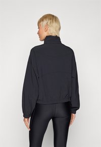 Chaqueta corta negra con un cuello alto, cintura elástica y mangas recogidas. Tejido suave y diseño minimalista sin herrajes visibles.